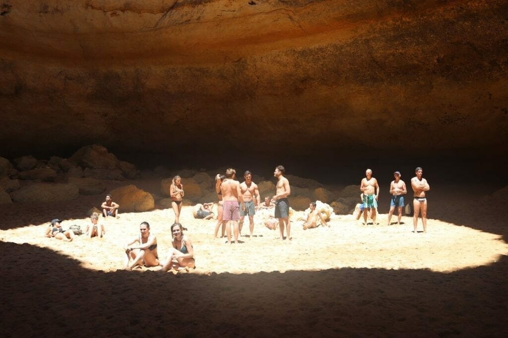 A group of people sunbathing inside Benagil Cave, Portugal, which has a round hole in the ceiling that allows the sun rays to get inside 