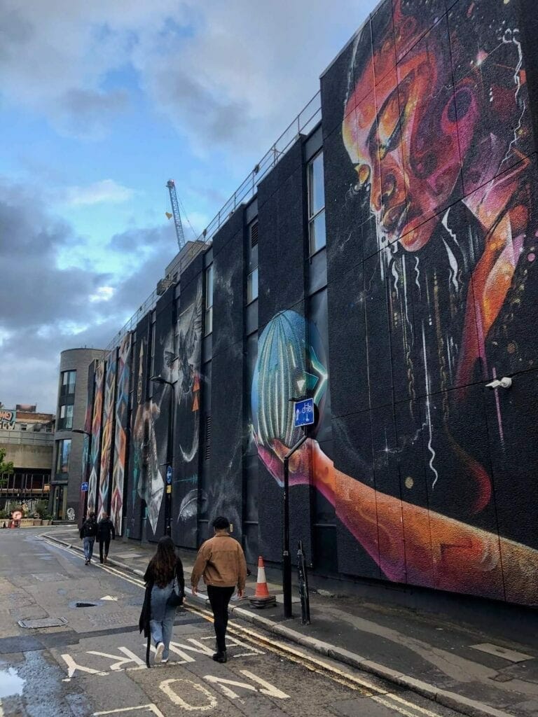 Cuatro personas caminando en New Inn Yard Street, en Shoreditch, Londres, y un edificio cubierto con un mural de graffiti