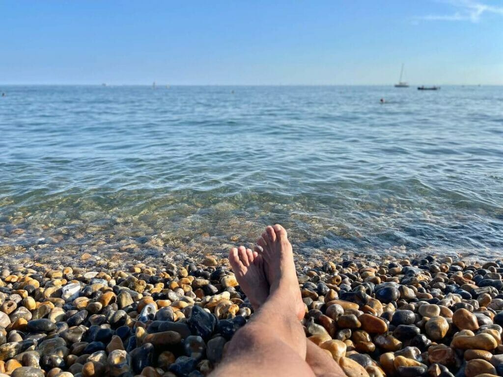 A pair of crossed legs laying down on the pebbles in front of the sea at Brighton Beach, England