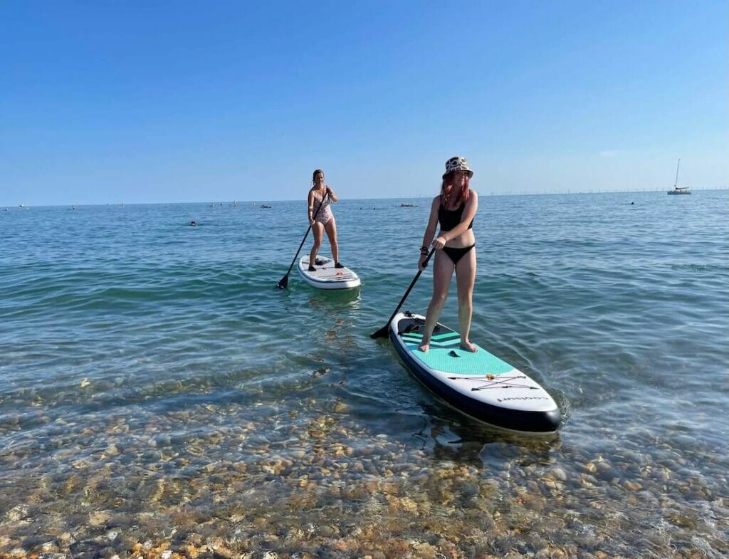 Two ladies doing stand up paddle boarding at Brighton Beach, Brighton, England