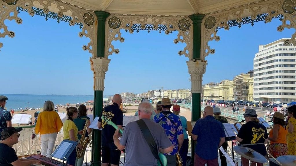 Um grupo de músicos de jazz se apresentando no The Bandstand em Brighton, com Brighton Beach e seu passeio ao fundo