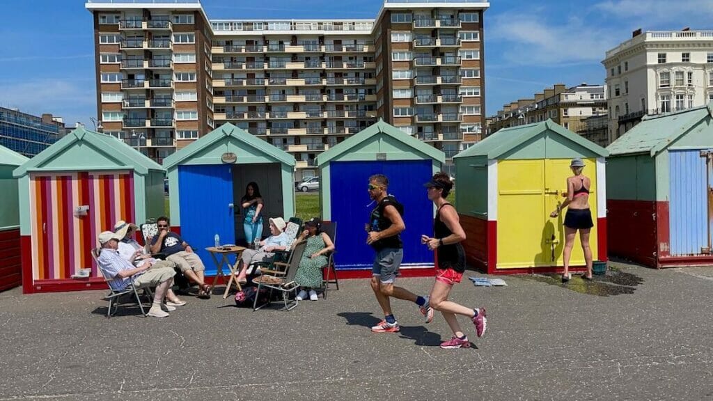 a couple running and other people sitting in front of some colourful beach huts in Hove