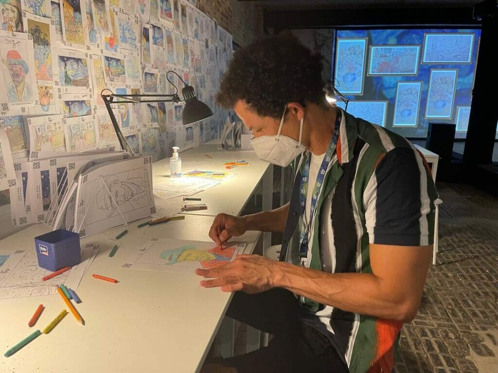 Pericles Rosa wearing a striped shirt and fa ace mask colouring a Van Gogh's portrait during the Van Gogh The Immersive Experience, London
