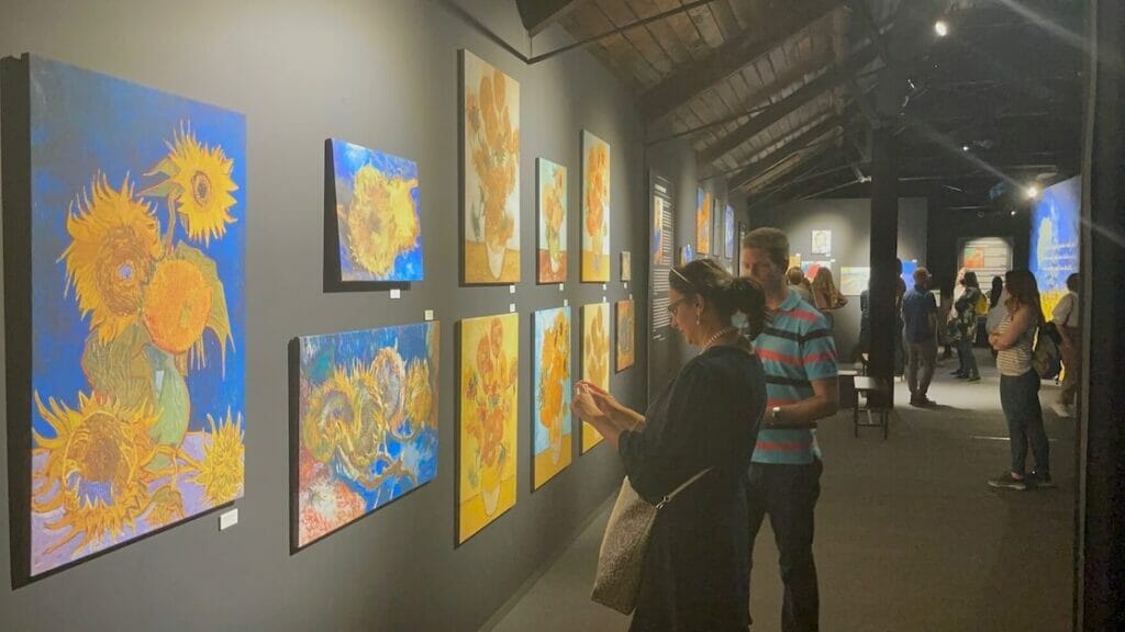 Uma galeria com algumas pessoas olhando para réplicas de pinturas de girassóis do Van Gogh, Londres