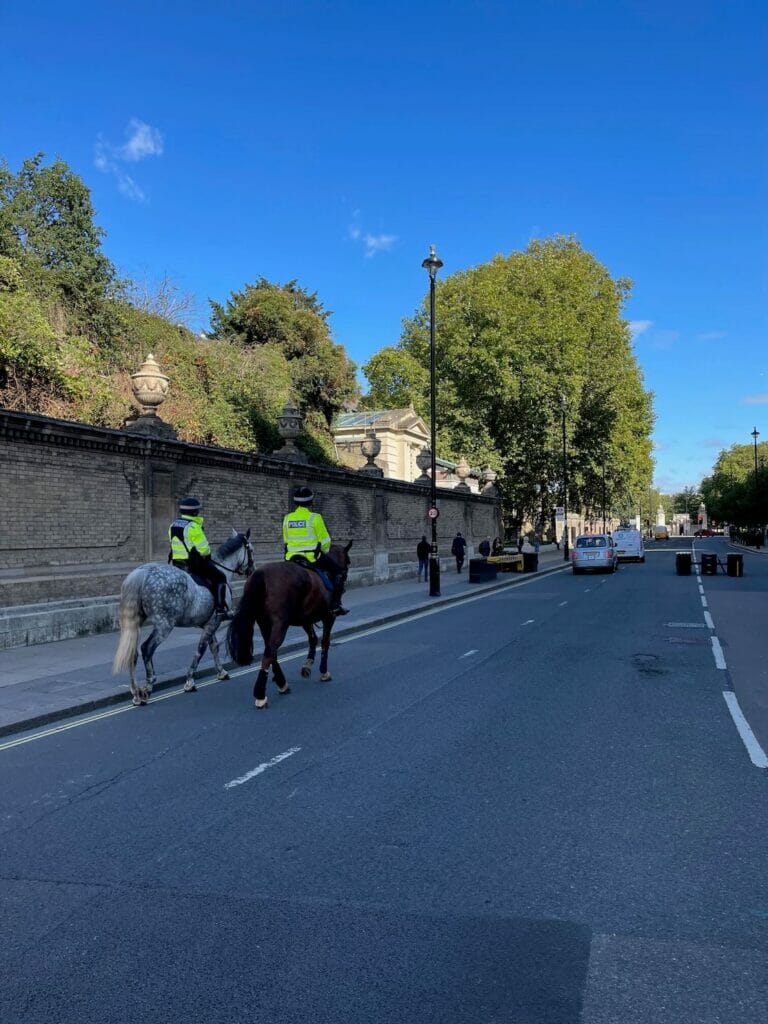 Two police men wearing green jackets horse riding on Buckingham Palace Road, London