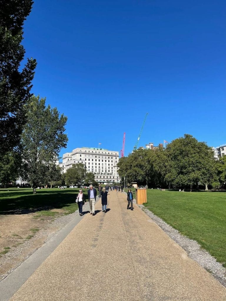 Pessoas andando no Green Park e algumas árvores e um prédio branco ao fundo, Londres