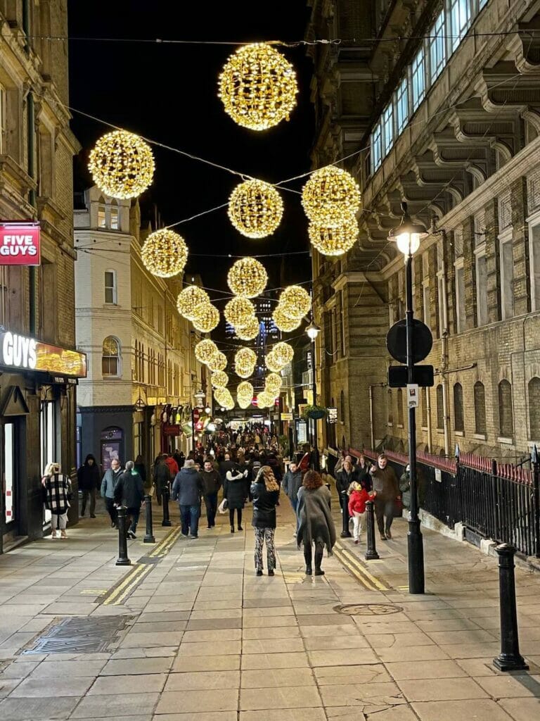 People walking on Villiers Street, London, which is decorated with Christmas lights