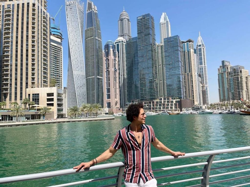 Péricles Rosa posando para uma foto no Dubai Marina Walk com alguns arranha-céus enormes como pano de fundo