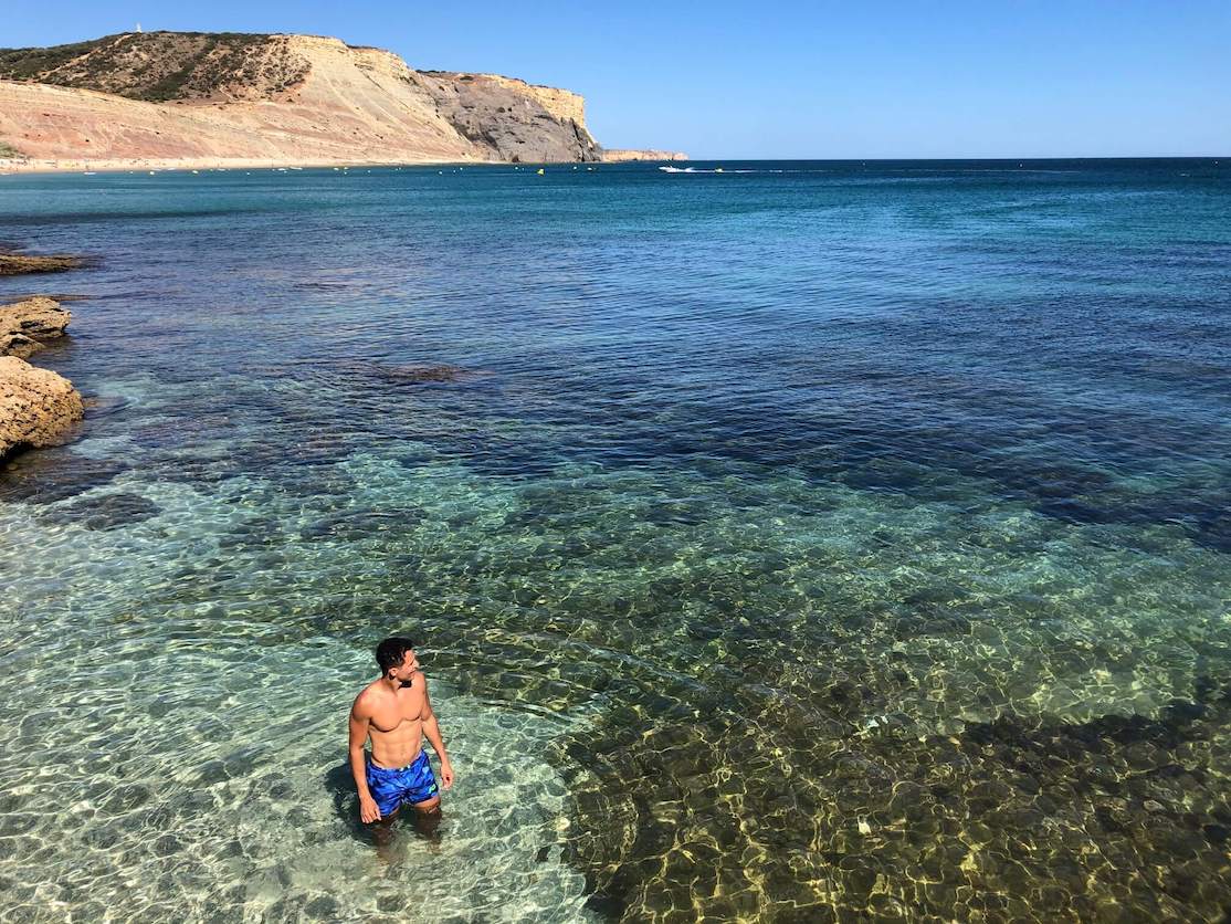 A man wearing a blue shorts in the crystalline water of Praia da Luz, Lagos, Portugal