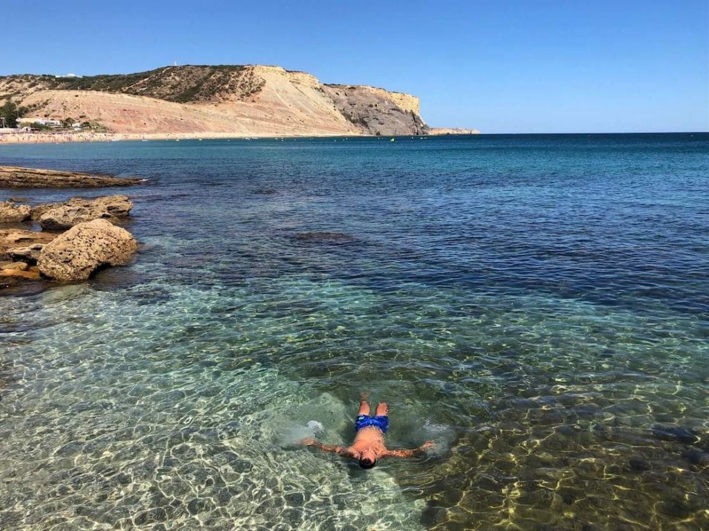 A man swimming in the crystal-clear water of Praia da Luz, Lagos, Portugal