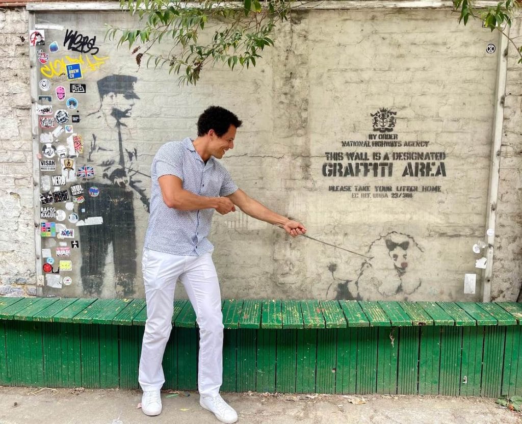 A man taking a picture in front the famous Guard Dog graffiti mural by Bansky on 83 Rivington Street, Shoreditch, London