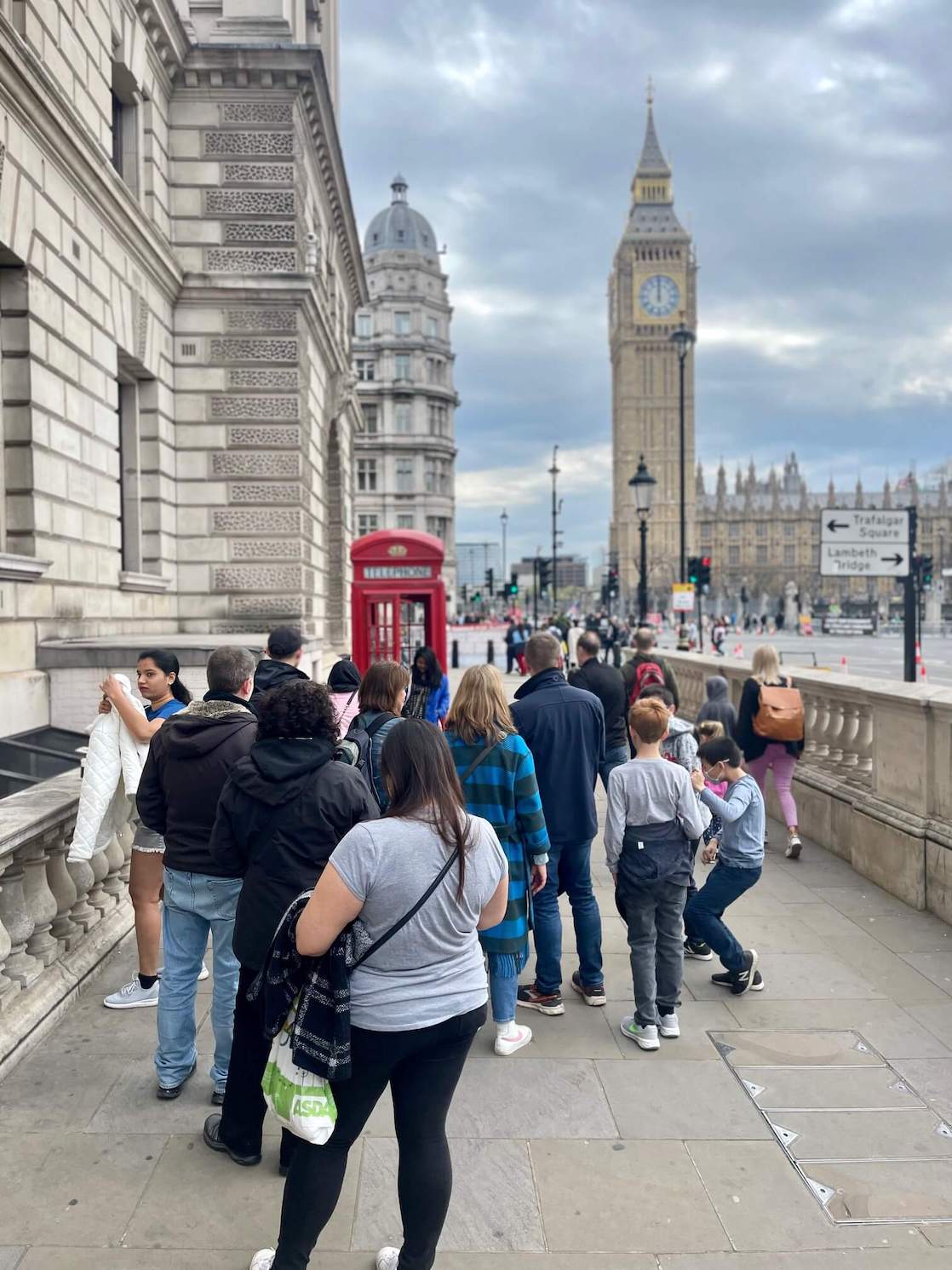 La gente haciendo una cola para sacar fotos en una cabina telefónica roja cerca del Big Ben en Londres