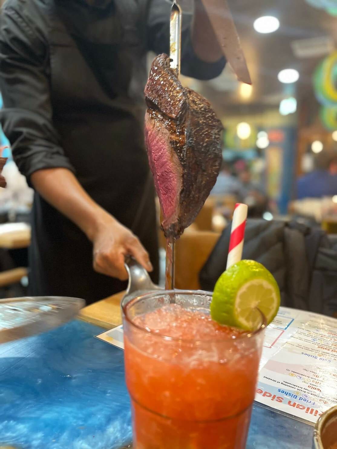 A glass of strawberry caipirinha and a piece of meat served during a rodizio at Preto Steakhouse, Soho, London