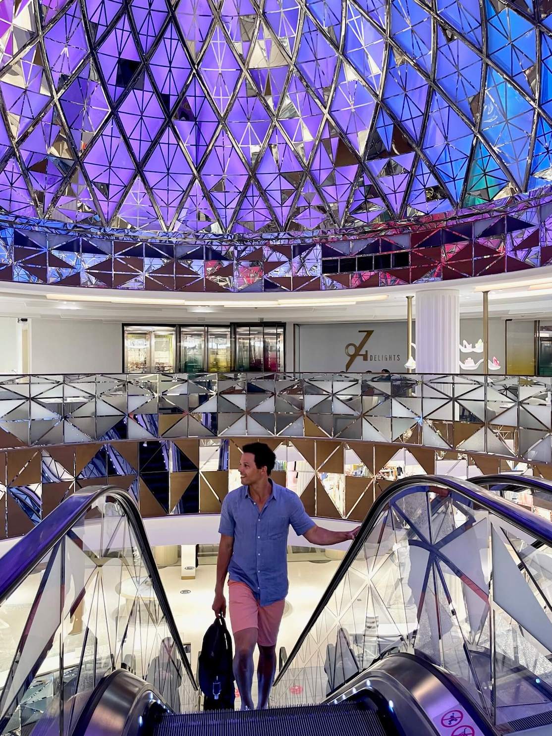 Un hombre en Galeries Lafayette, Doha, subiendo por las escaleras mecánicas con una cúpula de vidrio al fondo