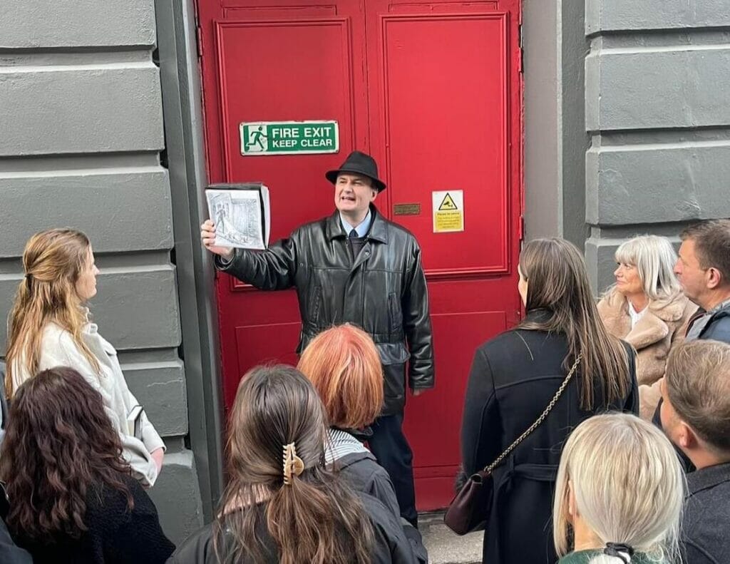 A tour guide is showing a picture of a police man finding the body of Jack the Ripper's first victim