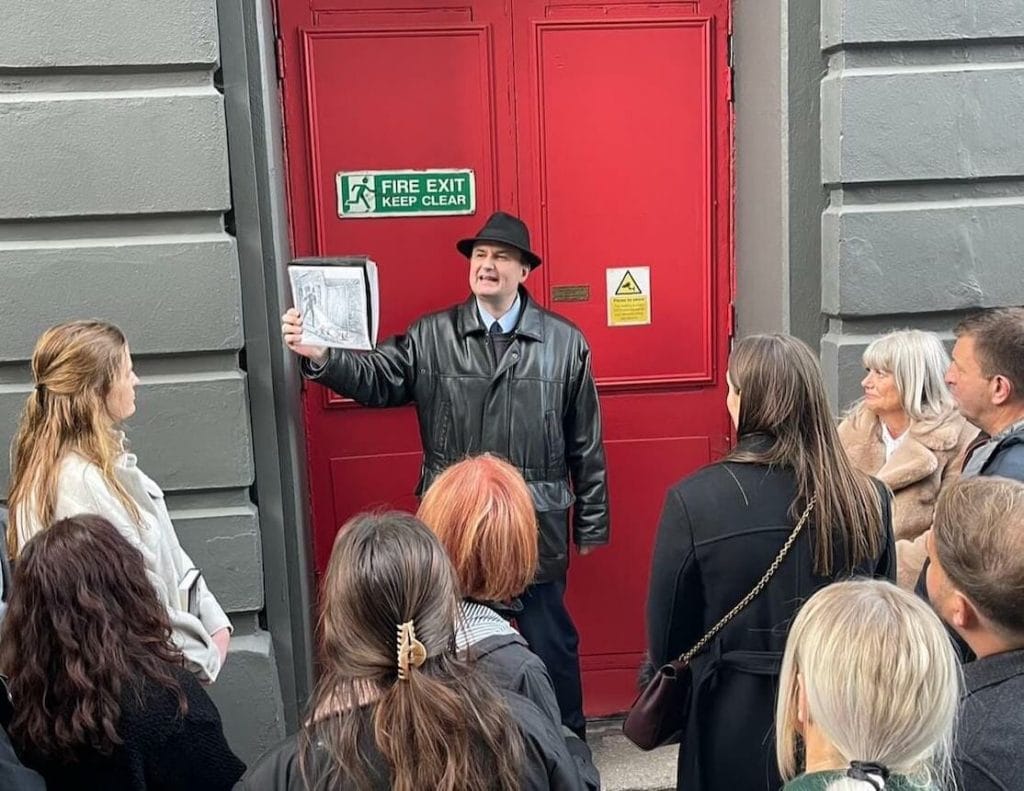 A tour guide is showing a picture of a police man finding the body of Jack the Ripper's first victim