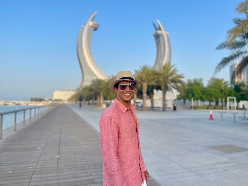 Péricles Rosa usando óculos escuros, chapéu e camisa de cor salmão, posando para uma foto no Lusail Marina Promenade, Qatar