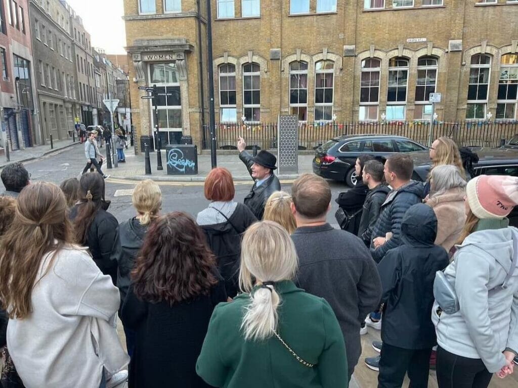 A tour guide is showing a building that was a convent to his group tour in Spitalfields, London