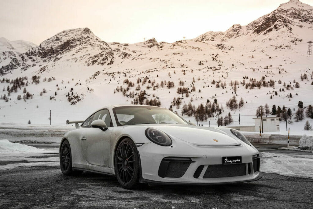 A Porsche 911 white on a road surrounded by snow-covered mountains 