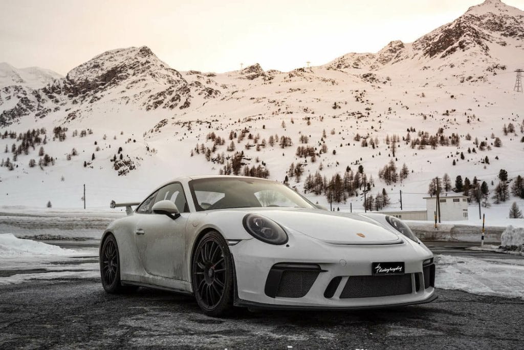 A Porsche 911 white on a road surrounded by snow-covered mountains 