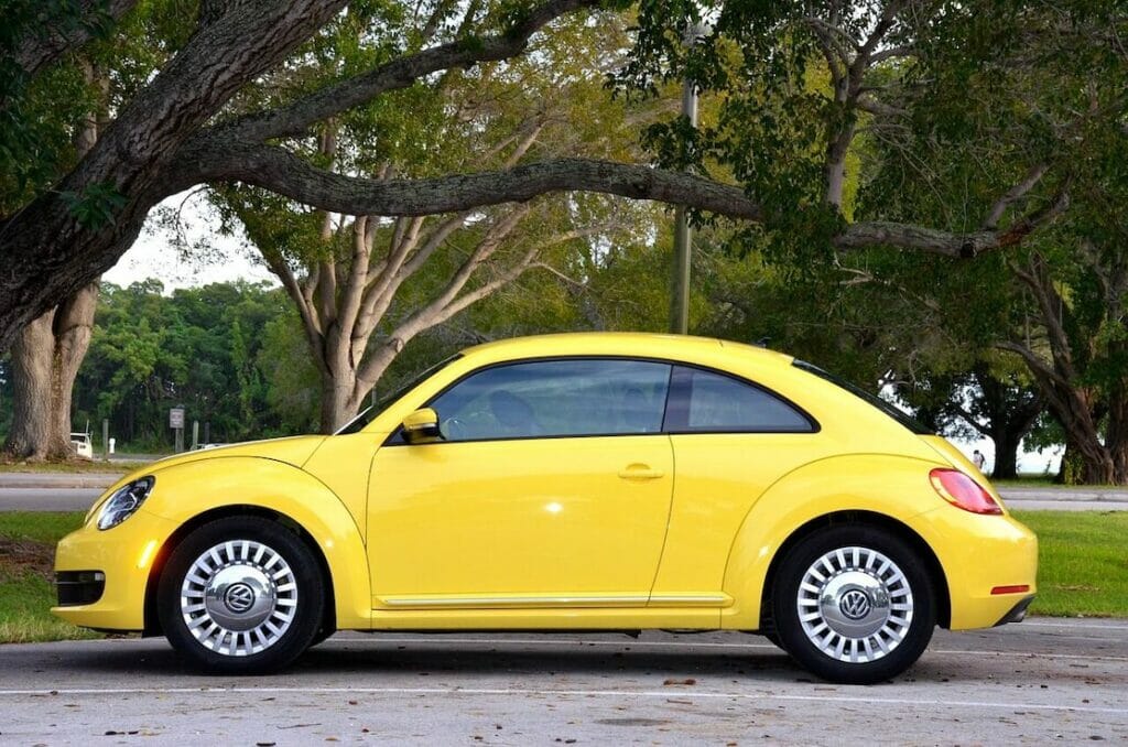 A Volkswagen Beetle yellow parked underneath a tree