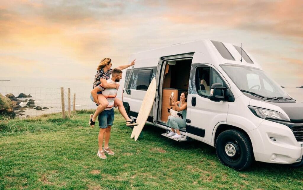 A sitting on the ledge of a campervan taking a picture of a couple