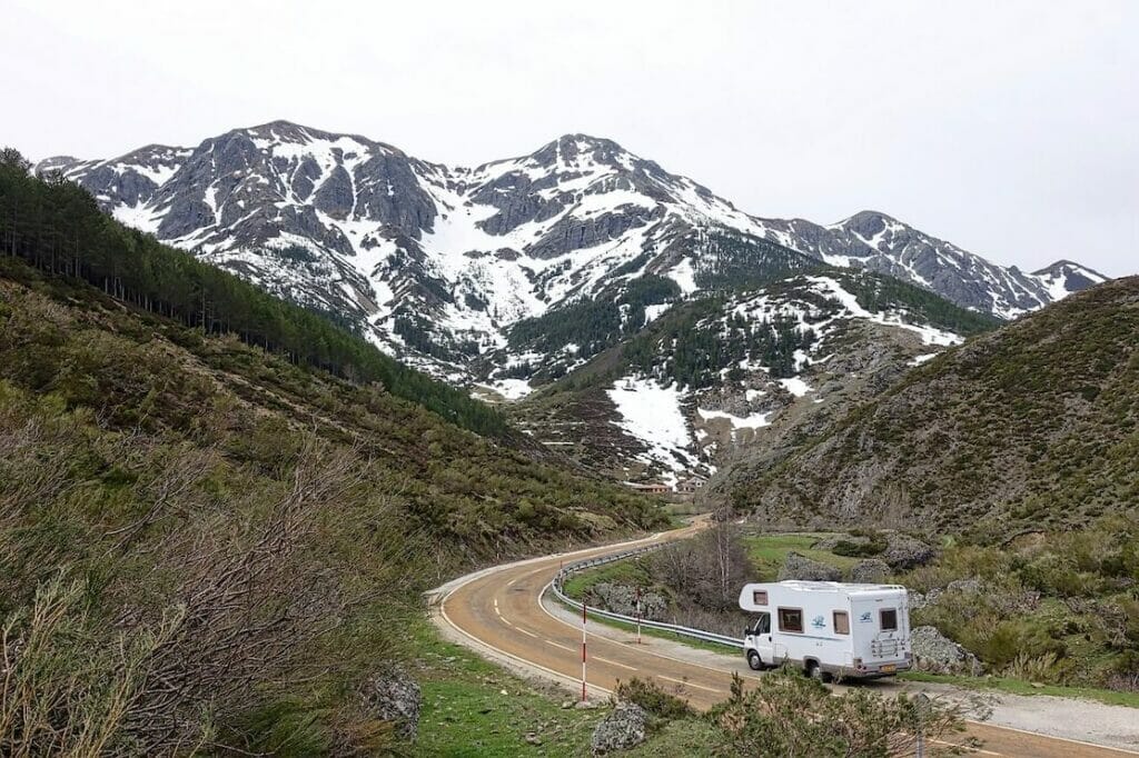 A motorhome driving on a road surrounded by mountains covered in snow