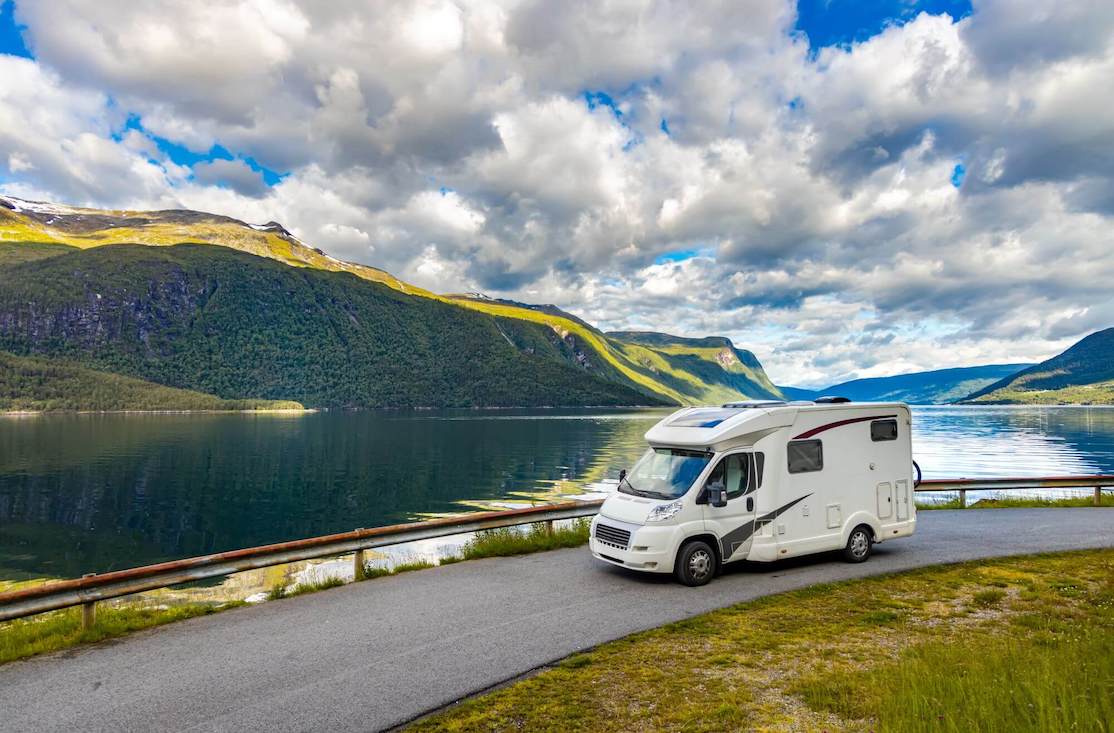 A campervan driving around a lake surrounded by mountains