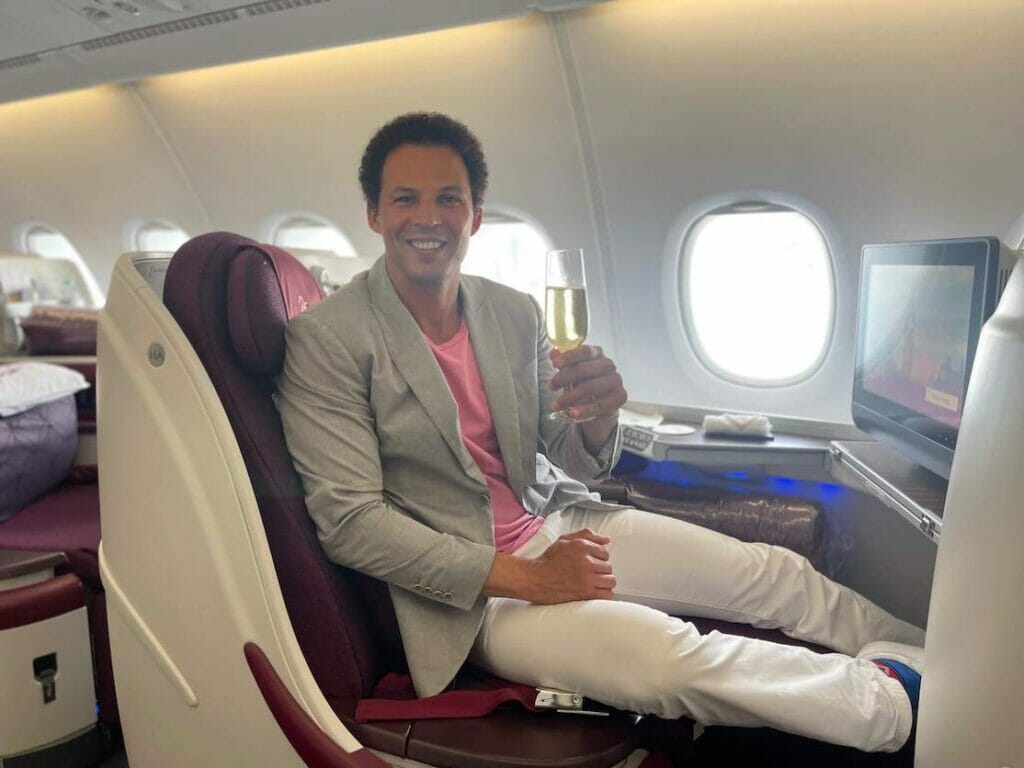 Péricles Rosa segurando uma taça de champanhe na classe executiva da Qatar Airways.