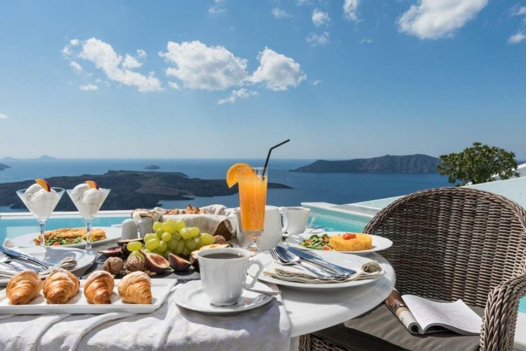 Desayuno servido junto a la piscina con la caldera y el mar Egeo de fondo en Anteliz Suites, Fira, Santorini