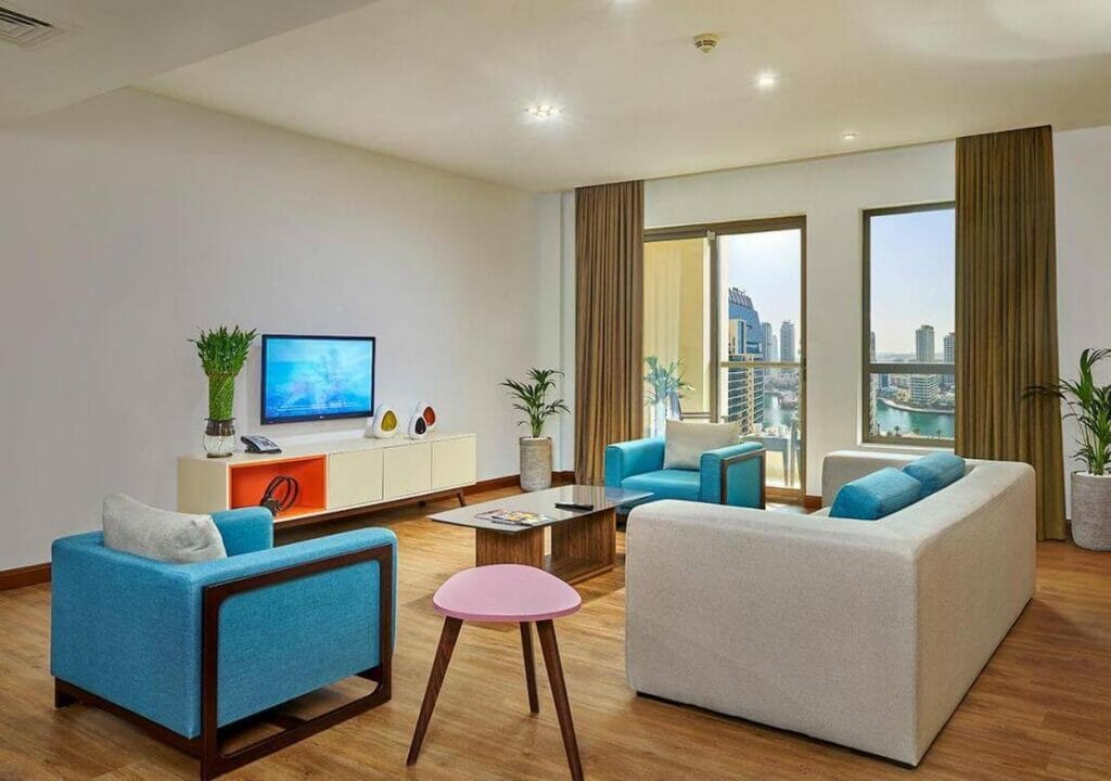 Um quarto com sofá, cadeiras, TV LCD e vista para a cidade no Ramada Hote & Suites no Jumeirah Beach Residence, Dubai