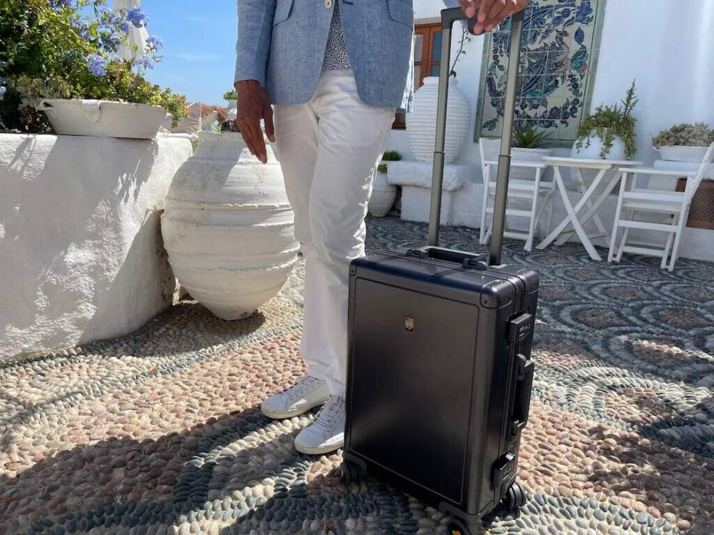 A man wearing a white trouser, light blue blazer and white sneakers carrying a full aluminium.