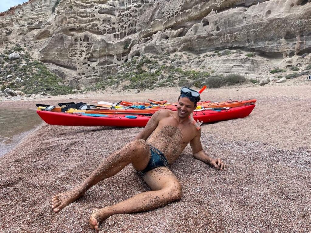 Un hombre en la arena de la Playa Roja con algunos kayaks detrás de él, Rodas, Grecia