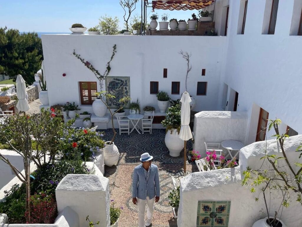 Um homem usando um chapéu branco, blazer azul claro e calça branca no Melenos Arty Boutique Hotel, Lindos, Rhodes, Grécia