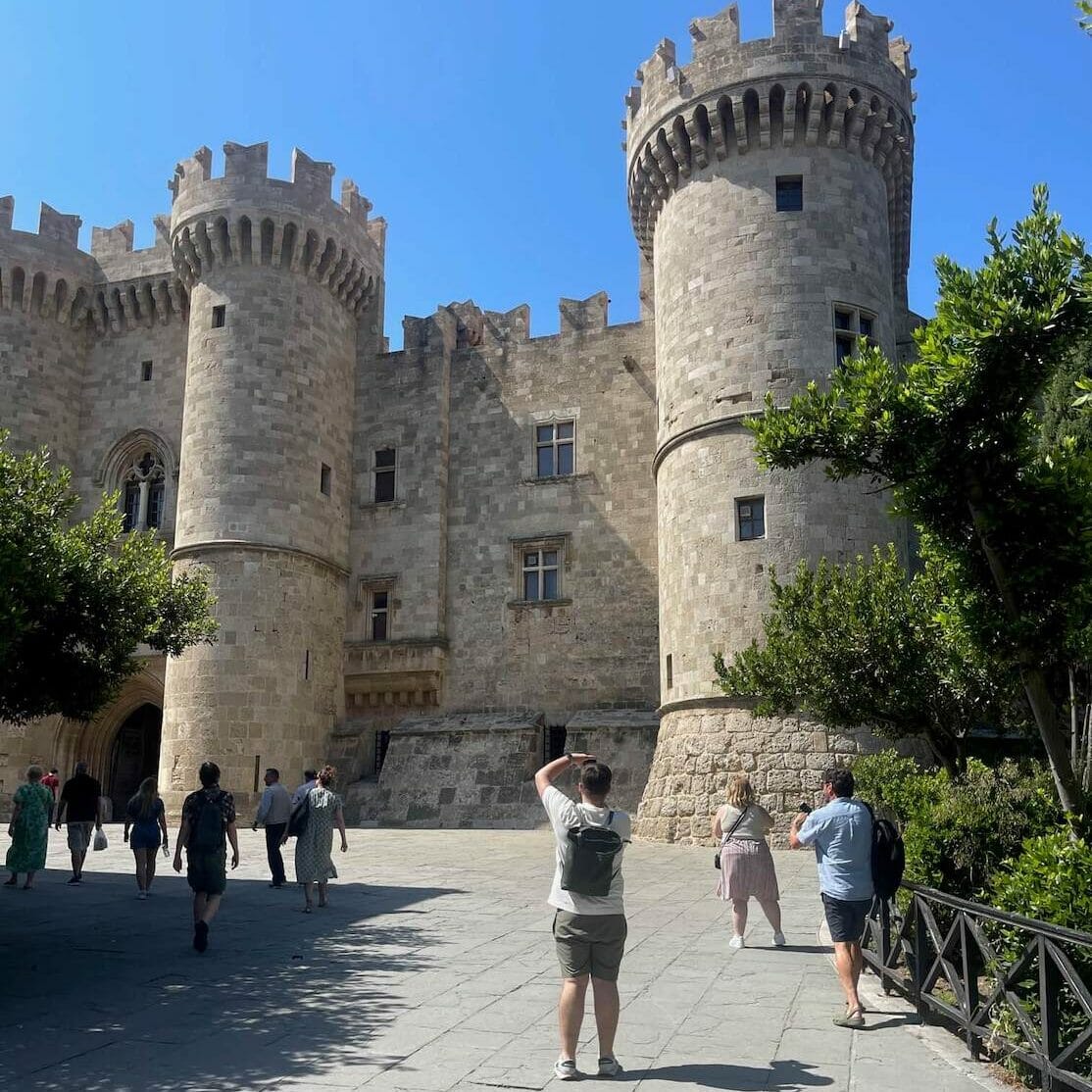 Pessoas tirando fotos e caminhando em frente à fachada do Palácio do Grão-Mestre dos Cavaleiros, Rodes, Grécia