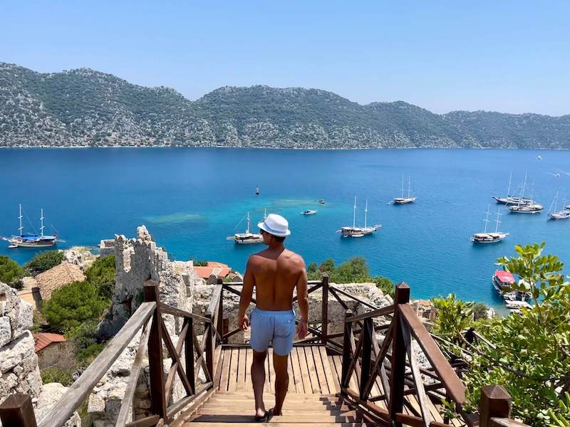 A man wearing a white had and light blue shorts admiring the view from Kekova Island Castle, Turkey