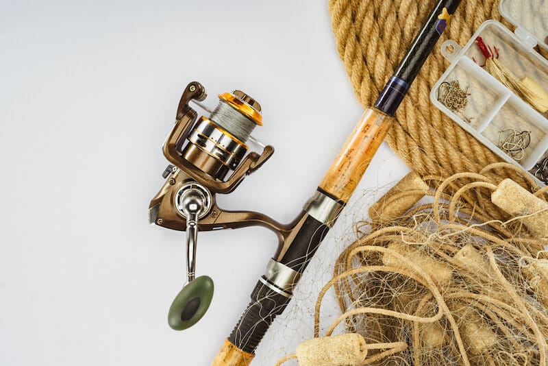 Top view of fishing rod, nautical rope, and plastic box with fishing tackle and bait isolated on white