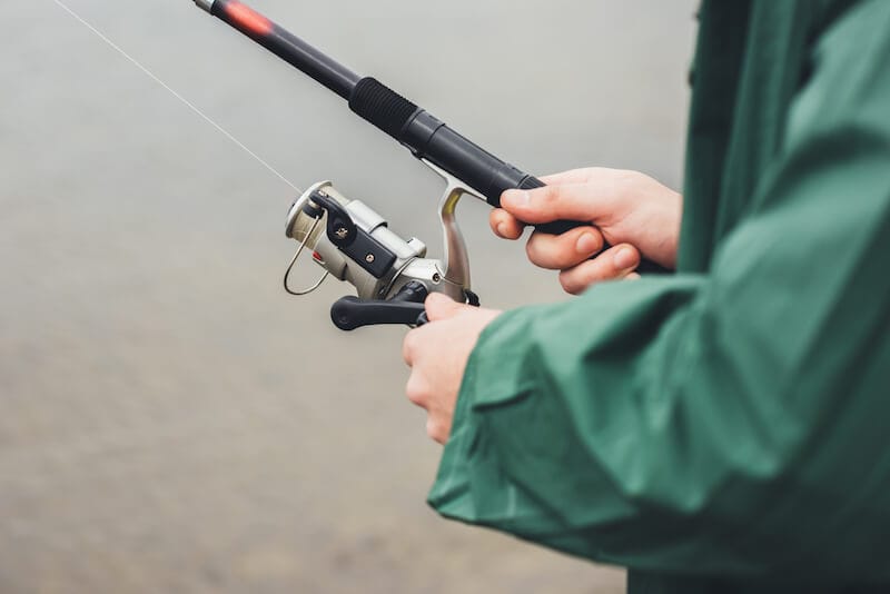 Cropped shot of a man in green raincoat holding fishing rod 