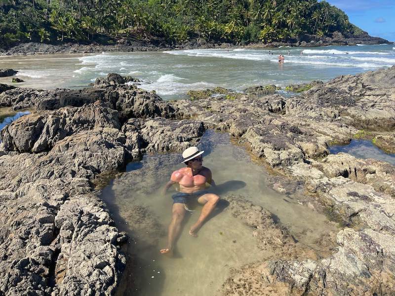 A man inside a natural formed by rocks with the sea and a hill covered in vegetation at Havaizinho Beach, Itacare, Bahia, Brazil