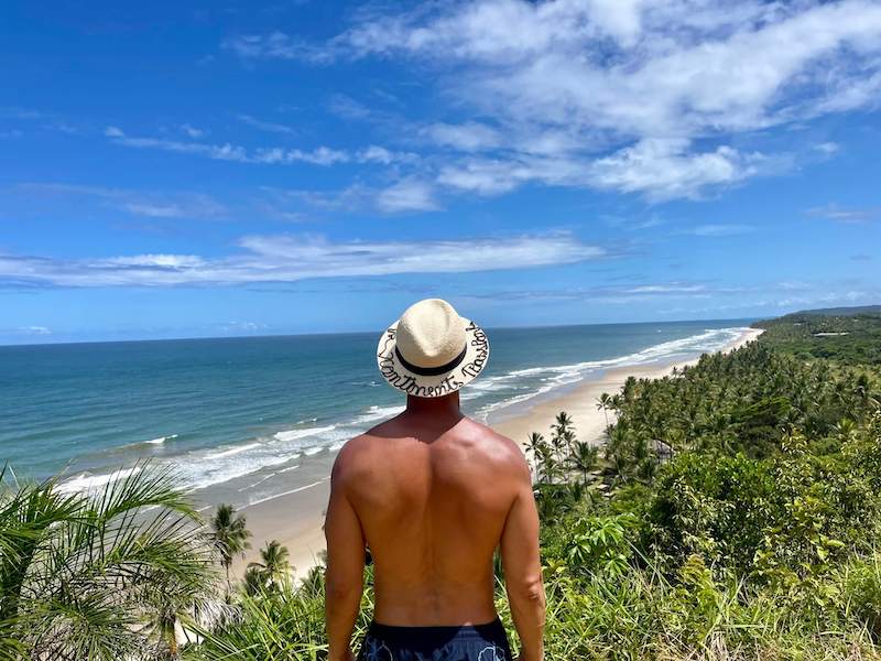 Un hombre con sombrero y pantalones cortos azules admirando la vista en el mirador de Itacarezinho, Itacaré, Brasil