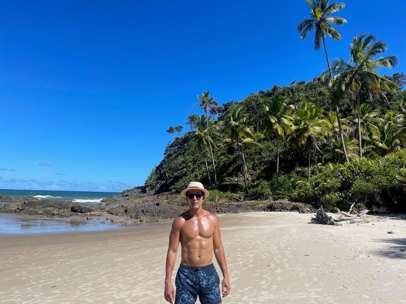 Péricles Rosa usando chapéu bege e bermuda azul posando para foto na Praia de Camboinha, Itacaré, Bahia, Brasil