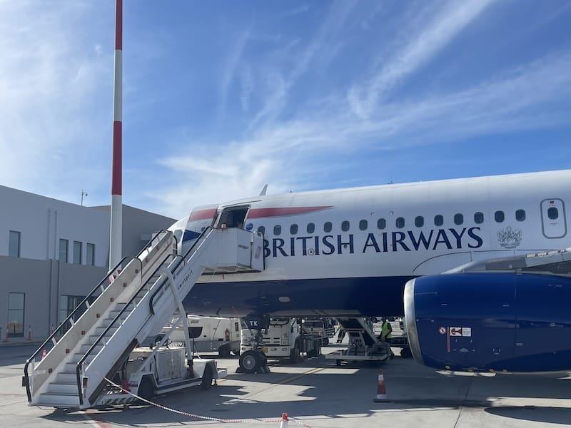 British Airways airplane parked at airport gate with boarding stairs and ground crew