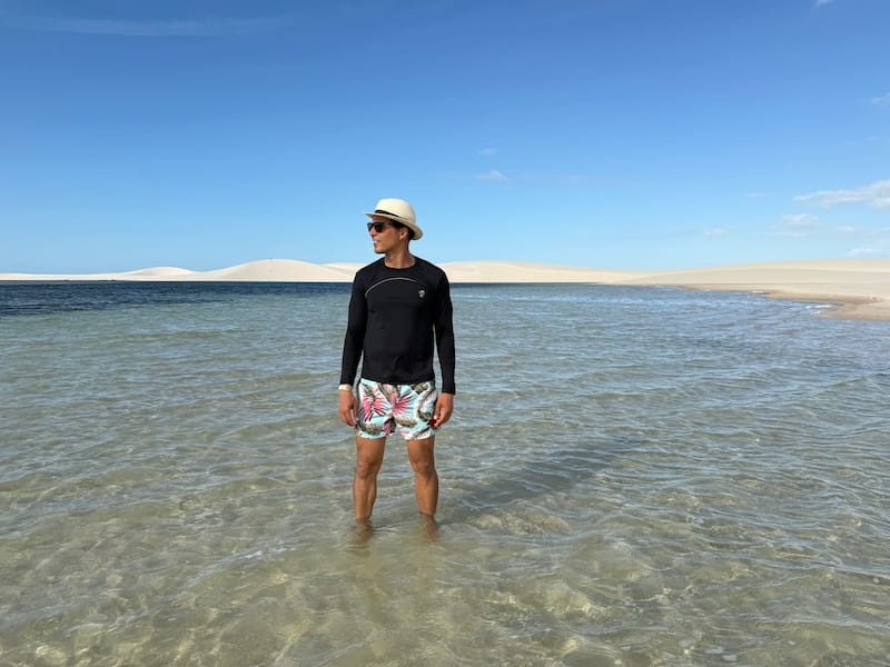 Man standing in crystal clear lagoon surrounded by sand dunes in Lençóis Maranhenses Brazil
